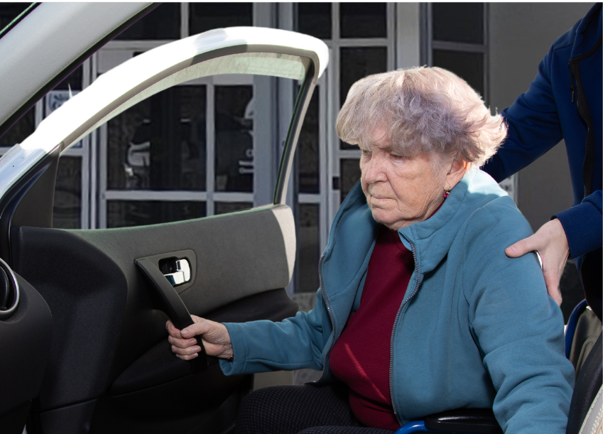 Image of an older woman being helped into her vehicle