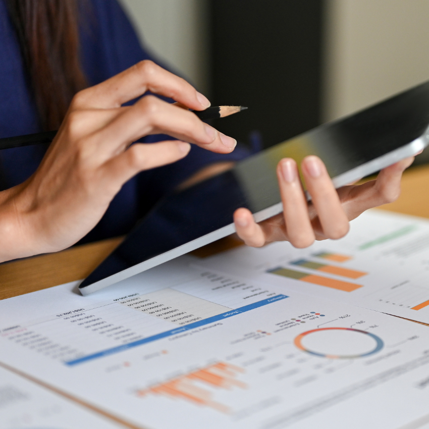 Image of a woman's hand holding a tablet with financial records on the table